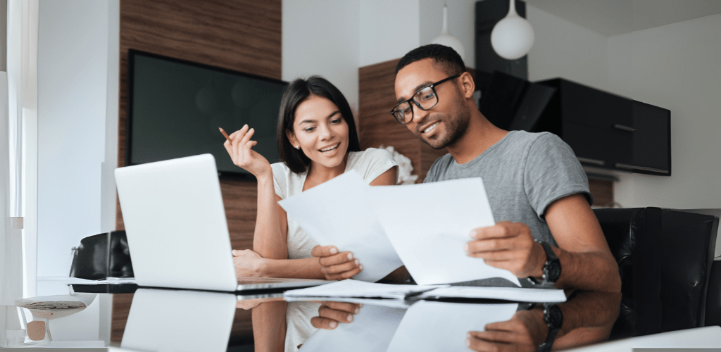 Man and woman sitting at desk looking through paper work with laptop open.